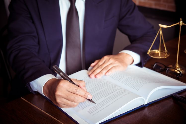 Man in a blue suit looking at a legal book with the scales of justice in the background